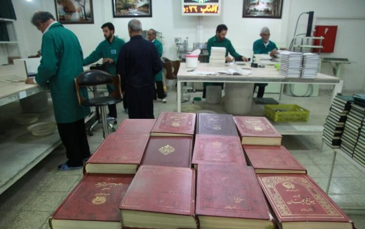 گوشه پله سنگی، زیارت‌نامه‌ای با جلد سرمه‌ای رنگ را برمی‌دارم اما قفسه کتاب‌ها خیلی از من دور است. بر فرض آنکه بتوانم حتی به کندی تا آن سوی صحن بروم، از میان این همه جمعیت معلوم نیست دوباره پای چند نفر را لگد خواهم کرد. به ناچار آن را روی لبه سنگی ایوان طلا می‌گذارم تا دست‌کم زیر دست و پا نماند. بانویی از آن سوی صحن صدایم می‌کند و اشاره می‌کند که زیارت‌نامه را به او بدهم. می‌فهمم عده‌ای از خدمه…